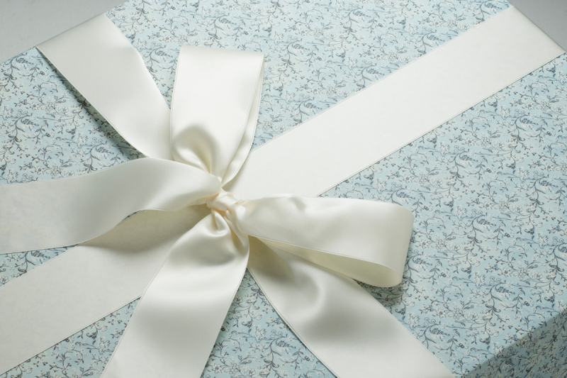 Die Brautkleidbox Blue Flower Dream wird mit einer passenden elfenbeinfarbenen Satinschleife kombiniert.